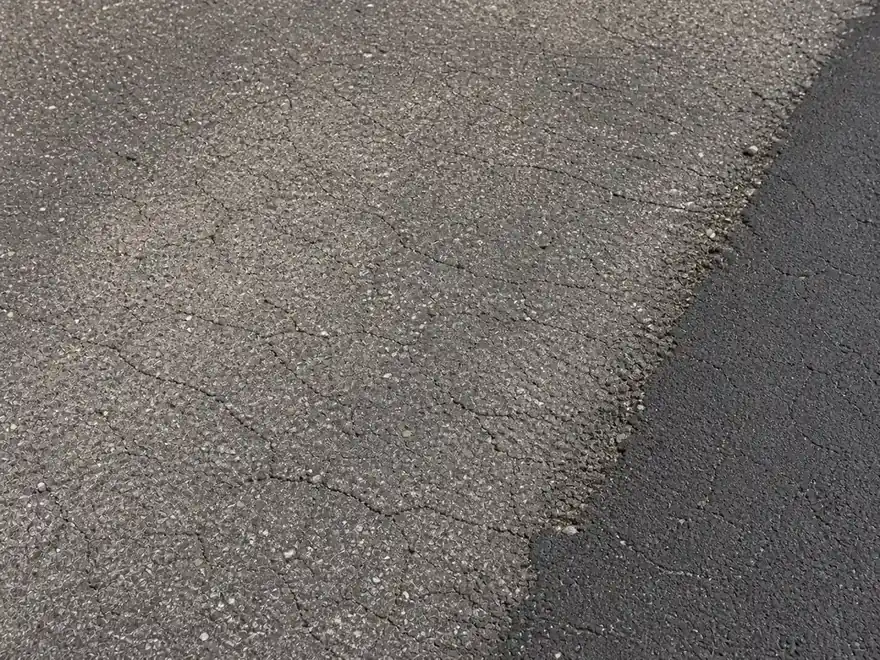 Weathered asphalt texture with fading, fine cracks, and raveling