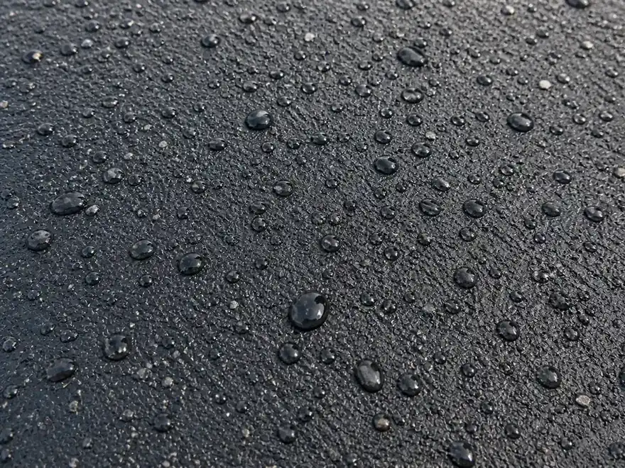 Water beads sitting on a dark sealcoated asphalt driveway surface